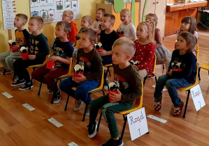 Dzieci siedzą na krzesełkach. W rękach trzymają kubeczki z popcornem.