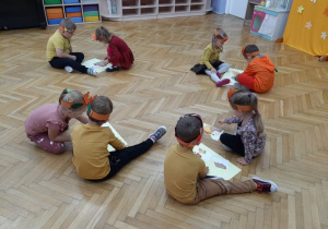 Dzieci siedzą na podłodze i układają w całość pocięte obrazki