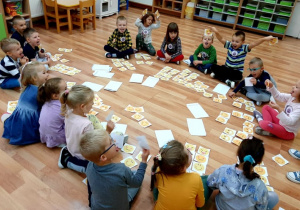 Dzieci siedzą na podłodze. Każdy ma kopertę w której są buźki z różnymi uśmiechami. Zadaniem dzieci jest dobranie w pary tych buziek.