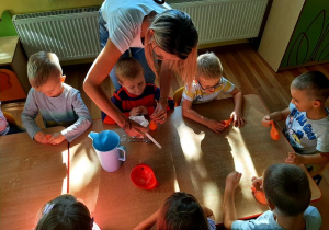 Chłopczyk z pomocą nauczycielki wsypuje przez lejek do balona mąkę a następnie strzykawką wlewa do niego wody.