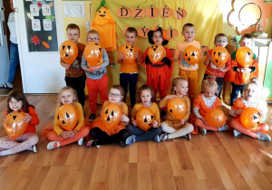 Grupowe zdjęcie dzieci. W rękach trzymają pomarańczowe balony, na które nakleiły oczy i nos, oraz dorysowały buzie.