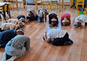 Przedszkolaki przykucnięte na podłodze ćwiczą prawidłową pozycję, w przypadku ataku psa