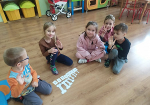 5 dzieci układa na podłodze kartonowe kości według wielkości i podpisuje je liczebnikami porządkowymi.