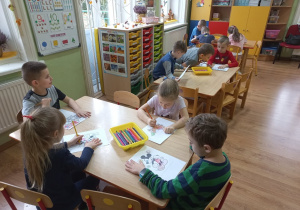 Przedszkolaki przy stolikach kolorują bajkowe postacie.