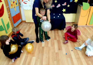 W balonach są umieszczone losy, na których jest napisane co prawdopodobnie w najbliższym czasie dzieci dostaną w prezencie. Przedszkolaki z pomocą nauczyciela przebijają szpilką balony.
