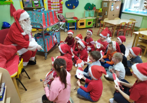 Dzieci siedzą przed Mikołajem i prezentują wykonane wcześniej prace - postać Mikołaja.