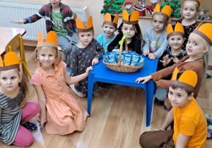 Przedszkolaki siedzą wokół niebieskiego stolika, na którym jest umieszczony koszyczek z ciasteczkami Misie Lubisie. Zaraz wszyscy zostaną nimi obdarowani.