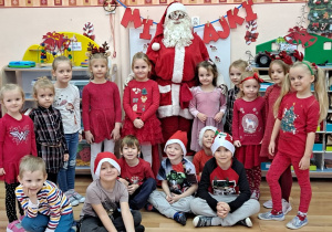 Mikołaj stoi z dziećmi na tle tablicy.