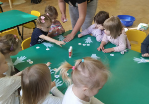 Dzieci układają trzy bakterie na szablonach dłoni i przyklejają je do niej.
