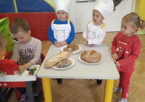 Dwoje dzieci ubrane w stroje kucharskie przedstawiające zawód piekarza, oraz drogę chleba do sklepu. Chłopiec będący sprzedawcą w przedszkolnym sklepiku, w którym to oczywiście przedszkolaki mogą kupić chleb.