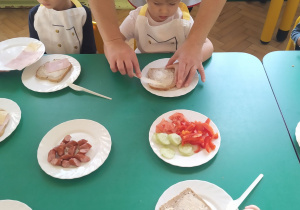 Dzieci smarują razowy chleb masłem, z niewielką pomocą pani Agnieszki