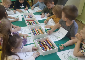 Dzieci siedzące przy stolikach kolorują kredkami liście buraka.