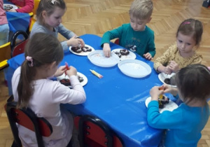 Dzieci przy stolikach dekorują pierniczki.