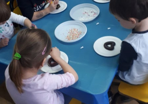 Dzieci przy stolikach dekorują pierniczki.