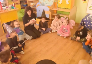 Nauczycielka opowiada dzieciom siedzącym w kole o tradycjach andrzejkowych.
