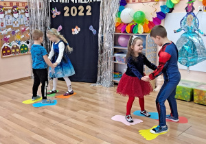 Dwie pary dzieci tańczą na kolorowych sylwetach stóp tak, aby z nich nie spaść