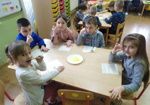 Dzieci siedzące przy stoliku zjadają miód z talerzyka.