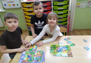 Dwóch chłopców i dziewczynka układają puzzle z Kubusiem Puchatkiem.