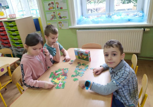 Troje dzieci przy stoliku układa puzzle z Kubusiem.