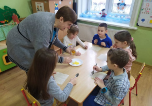 Nauczycielka nakłada na talerzyk miód do degustacji dla dzieci.
