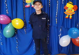 Chłopiec w stroju policjanta na tle dekoracji karnawałowej.