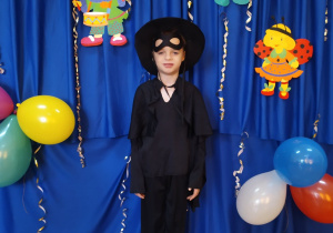 Chłopiec w przebraniu Zorro na tle dekoracji karnawałowej.