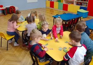 Dzieci układają puzzle przy stolikach.