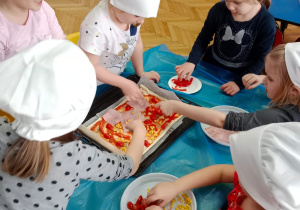 Dzieci dekorują placki pizzy.