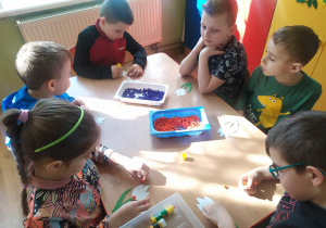 Dzieci przy stoliku wyklejają szablon krokusa kuleczkami bibuły.