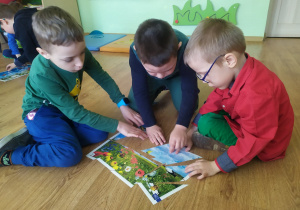 Trzech chłopców układa obrazek pocięty na części, przedstawiający wiosenna łąkę.