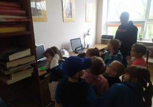 Pan bibliotekarz przy komputerze zapoznaje dzieci ze sposobem księgowania książek.