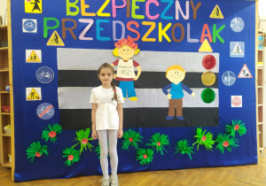 Dziewczynka na tle dekoracji z napisem "Bezpieczny przedszkolak".