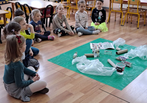 Przed "Misiami" siedzącymi w półkolu leżą porozrzucane śmieci.