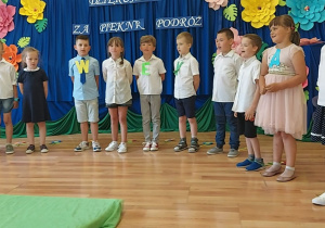 Dzieci w półkolu śpiewają piosenkę pt. "W przedszkolu było super".