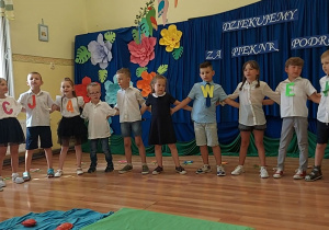 Dzieci trzymają się za ręce i śpiewają piosenkę.