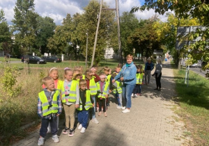 Dzieci oglądają znaki ustawione na chodniku i słuchają objaśnień nauczycielki.