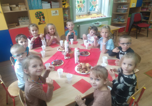 Grupa przedszkolaków siedzi przy stole podczas słodkiego poczęstunku.