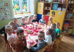 Grupa dzieci siedzi przy stoliku podczas słodkiego poczęstunku.