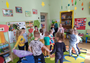 Grupa dzieci tańczy przy muzyce z chustami w rączkach.