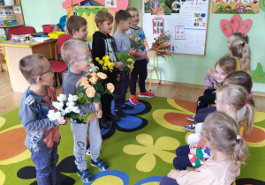 Chłopcy trzymają w rączkach bukiety kwiatów i śpiewają koleżankom "Sto lat".