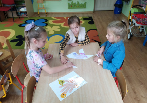 Trzy dziewczynki układają puzzle przedstawiające dłoń z zarazkami.