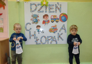 Chłopcy pozują do zdjęcia z papierowymi krawatami, na tle napisu "Dzień Chłopaka"