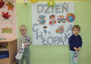 Chłopcy pozują do zdjęcia z papierowymi krawatami, na tle napisu "Dzień Chłopaka"