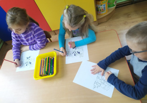 Troje dzieci podczas kolorowania bajkowych obrazków.