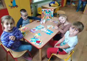 Czwórka dzieci układa na stoliku bajkowe puzzle.