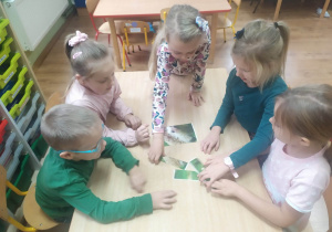 Grupa dzieci układa na stole puzzle przedstawiające jeża.