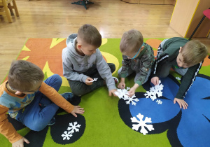 Grupa chłopców układa śnieżynki w ustalonej kolejności od największej do najmniejszej i przelicza je.