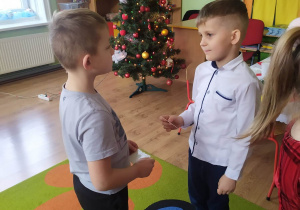 Dwóch chłopców dzieli się opłatkiem i składa sobie świąteczne życzenia.
