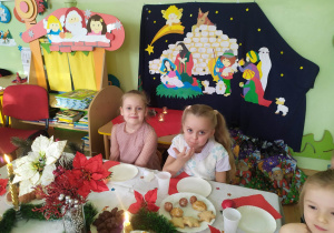 Dzieci przy stole wigilijnym na tle szopki betlejemskiej.