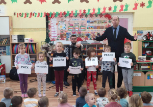 Pan Maciek z grupą dzieci trzymającą w rękach kartki z napisem "Pokój" w różnych językach świata.